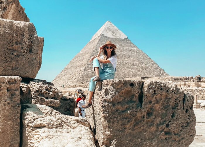 A wonderful picture of a girl sitting on a rock in front of the Giza Pyramids