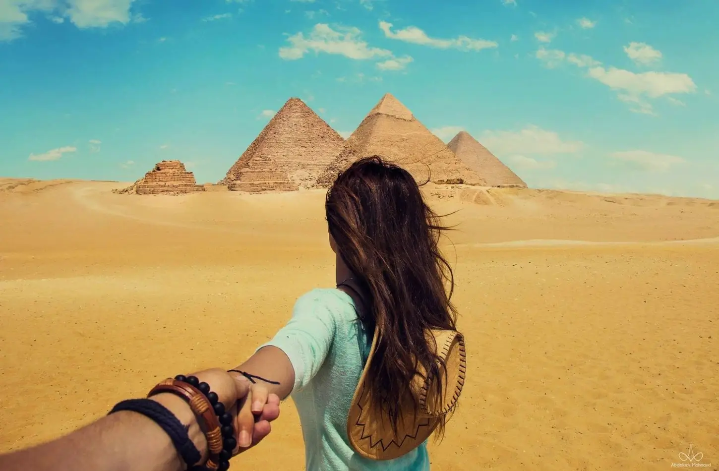 A couple holds hands while walking toward the Giza plateau to learn the history of how ancient Egyptians built the pyramids.