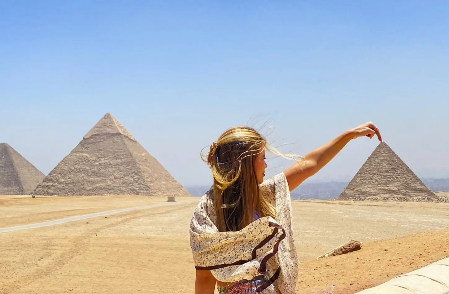 A tourist poses at the Giza plateau with a perspective trick, seemingly touching the peak of a pyramid, while visiting the area surrounding the Best Museums in Cairo Egypt.