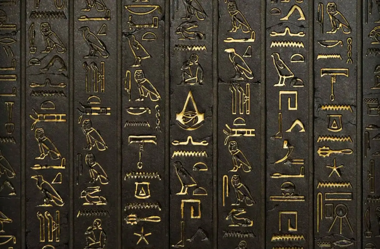 A dark, textured stone wall featuring vertical columns of golden Ancient Egypt symbols, including owls, birds, and an Eye of Horus framed by a stylized crest.