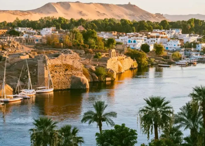 Scenic sunset over the Nile River in Aswan with traditional felucca boats and ancient ruins, illustrating the best time for a Nile cruise in Egypt.