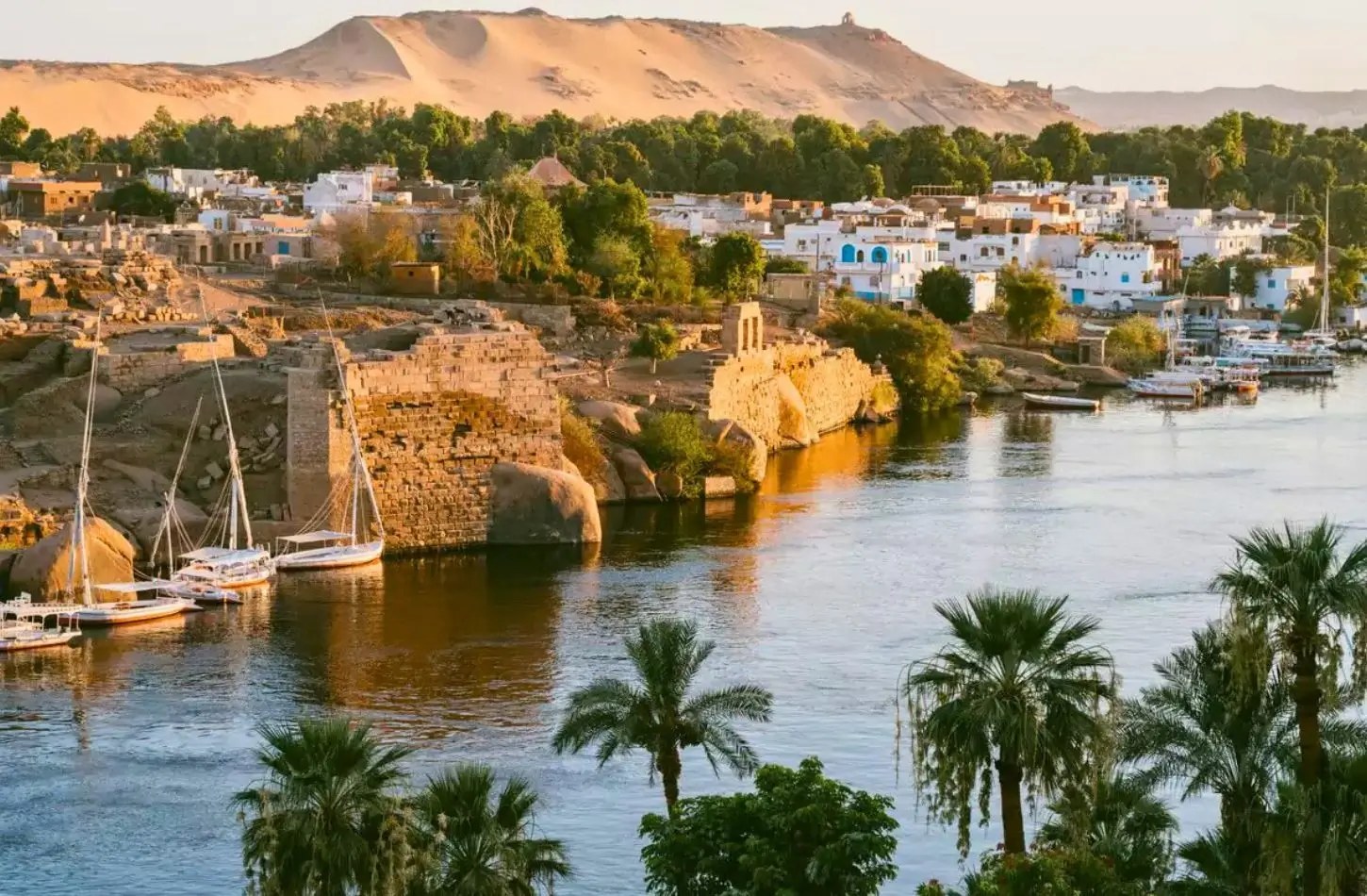 Scenic sunset over the Nile River in Aswan with traditional felucca boats and ancient ruins, illustrating the best time for a Nile cruise in Egypt.
