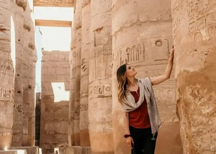 A woman gazes up at massive, hieroglyphic-covered pillars in an ancient temple, highlighting the rich history that makes travelers ask, "Do You Need a Tour Guide in Egypt?"
