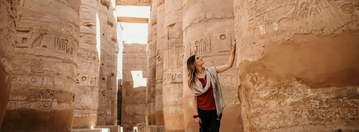 A woman gazes up at massive, hieroglyphic-covered pillars in an ancient temple, highlighting the rich history that makes travelers ask, "Do You Need a Tour Guide in Egypt?"