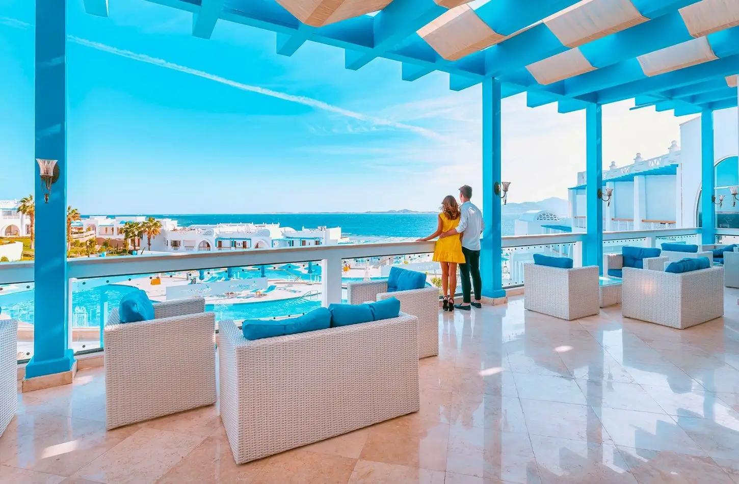 A couple looks out over a bright blue luxury resort swimming pool and the ocean from a modern balcony, a relaxing finale for an Egypt itinerary 7 days.