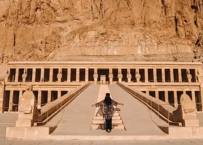 A traveler walking up the central ramp toward the towering columns of the Mortuary Temple of Hatshepsut in Luxor, Egypt