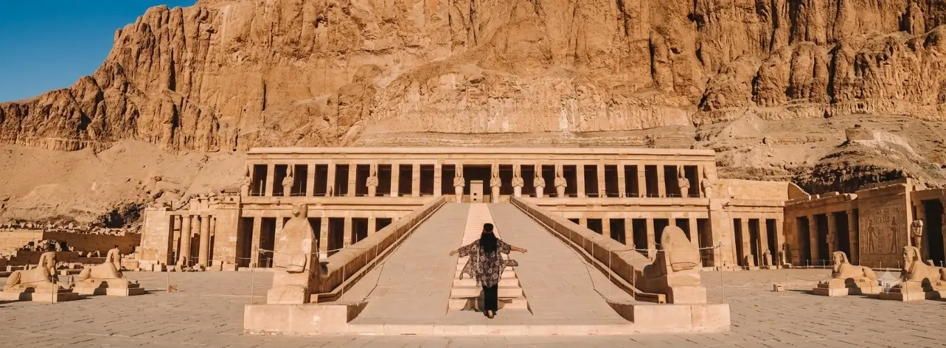 hatshepsut-temple-luxor-travel-guide A traveler walking up the central ramp toward the towering columns of the Mortuary Temple of Hatshepsut in Luxor, Egypt