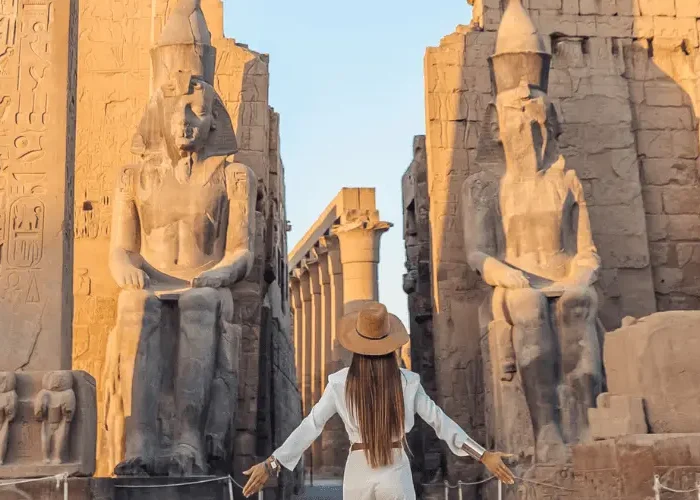 A female traveler in a white jumpsuit and sun hat standing before the ancient giant statues at the entrance of Luxor Temple in 5 Day Egypt Itinerary