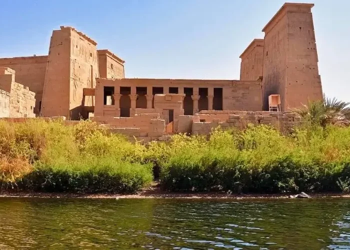 Panoramic view of the ancient Egyptian Philae Temple complex on Agilkia Island, seen from the Nile River in Aswan under a clear blue sky.