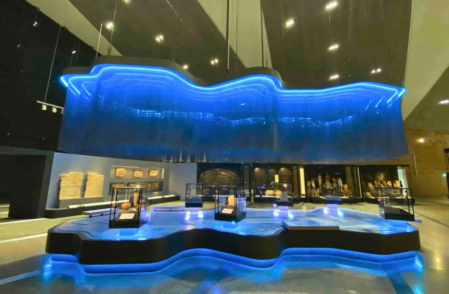 An innovative, high-tech gallery layout inside the Grand Egyptian Museum utilizing dramatic blue LED light installations to highlight historical artifact display cases.