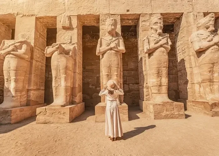 A tourist in a white dress stands before ancient Osiride statues at Medinet Habu temple during a trip to Egypt in November.