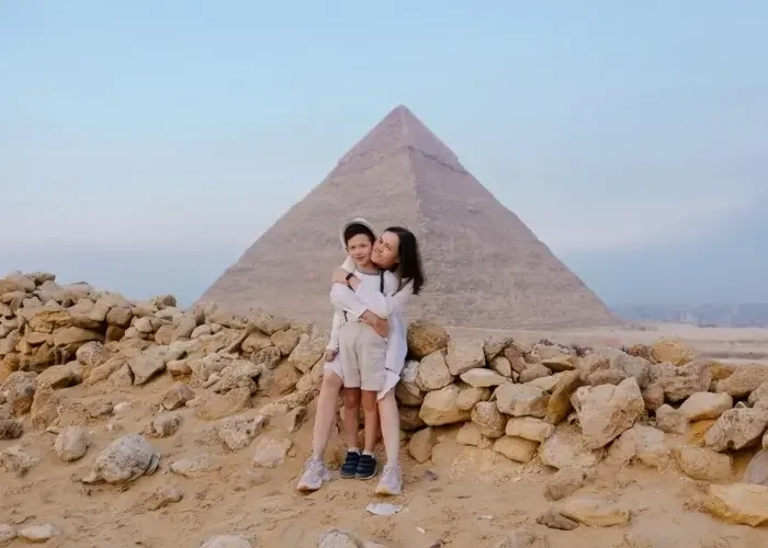 A mother hugging her son while sitting on a stone wall in the desert with the majestic Great Pyramid of Giza behind them, a highlight of a family friendly Egypt itinerary 10 days