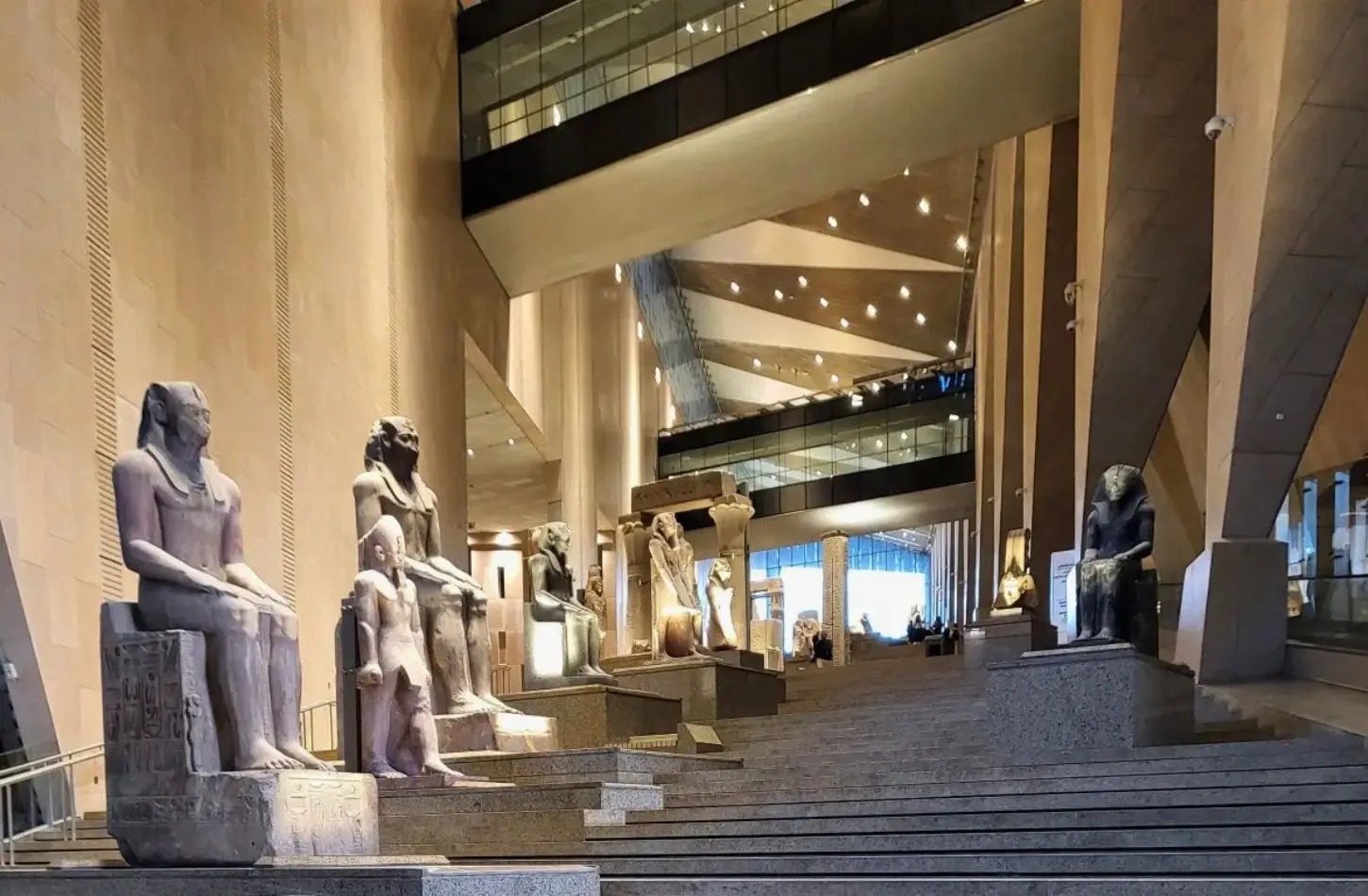 A row of monumental stone pharaoh statues lining the tiered grand staircase exhibition area inside the modern interior of the Grand Egyptian Museum.