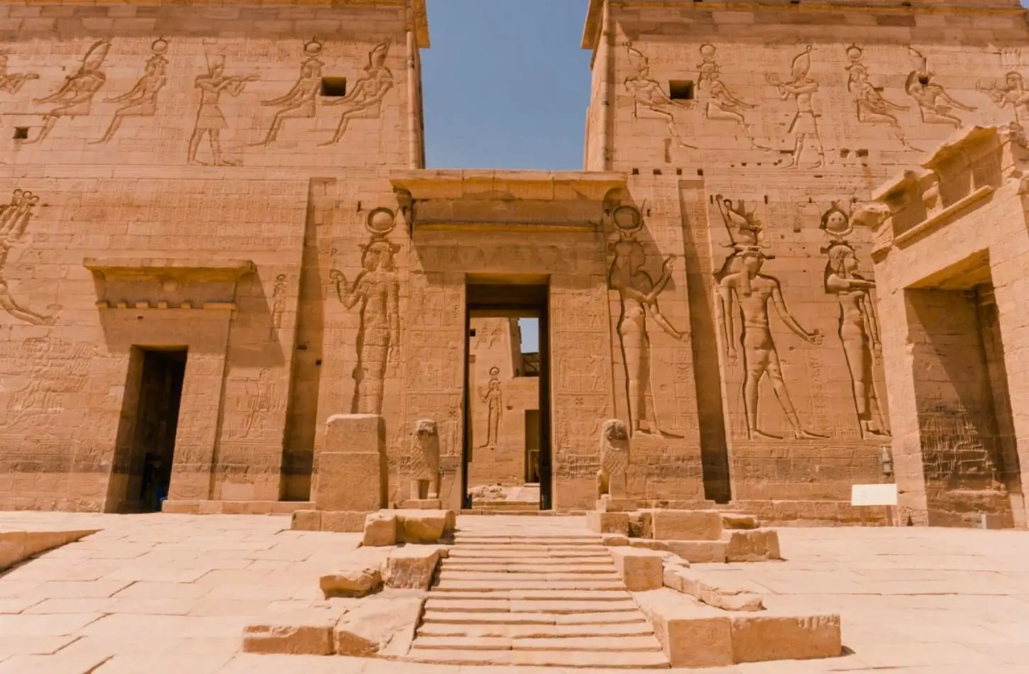 Daytime view of the Second Pylon at the Philae Temple complex in Aswan, Egypt, featuring large relief carvings of ancient Egyptian deities flanking the central doorway.