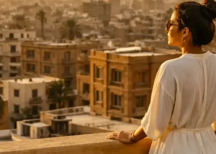 Egypt in September: A scenic view of city roofs and palm trees from a rooftop during golden hour with a woman looking into the distance.