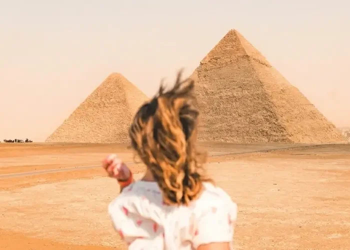 Woman running through the desert towards the Great Pyramids of Giza while exploring Egypt in January