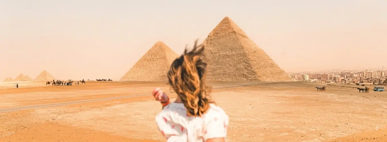 tourist-running-towards-giza-pyramids-cairo Woman running through the desert towards the Great Pyramids of Giza while exploring Egypt in January