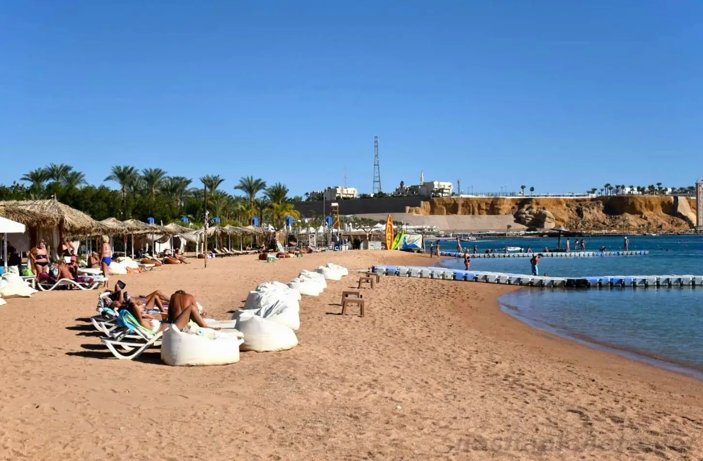 Egypt in September: Tourists relaxing on sun loungers and bean bag chairs along a sandy beach at a coastal resort.