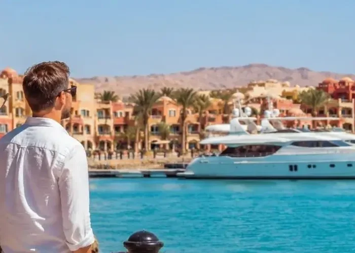 A couple standing on a waterfront promenade looking out over a luxury marina with yachts and colorful resort architecture, showcasing popular things to do in Hurghada.