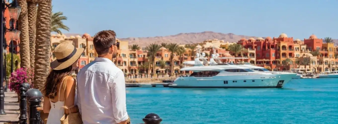 couple-vacation-luxury-marina-resort A couple standing on a waterfront promenade looking out over a luxury marina with yachts and colorful resort architecture, showcasing popular things to do in Hurghada.