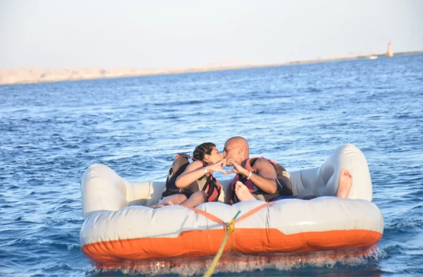 A couple kissing and making a heart shape with their hands while riding a towed inflatable tube, highlighting fun water sports and exciting things to do in Hurghada.