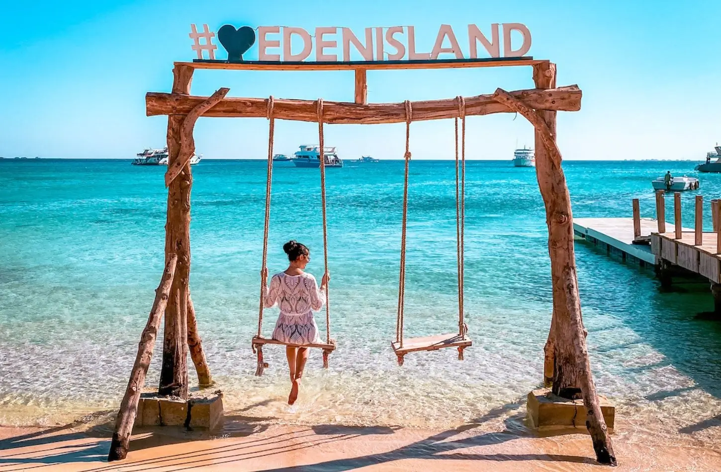A woman sitting on a wooden beach swing over clear turquoise water at Eden Island, highlighting relaxing tropical things to do in Hurghada.