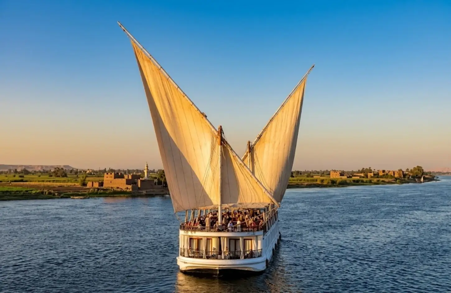 Traditional wooden dahabiya boat sailing along the Nile River under clear skies during a vacation in Egypt in February.