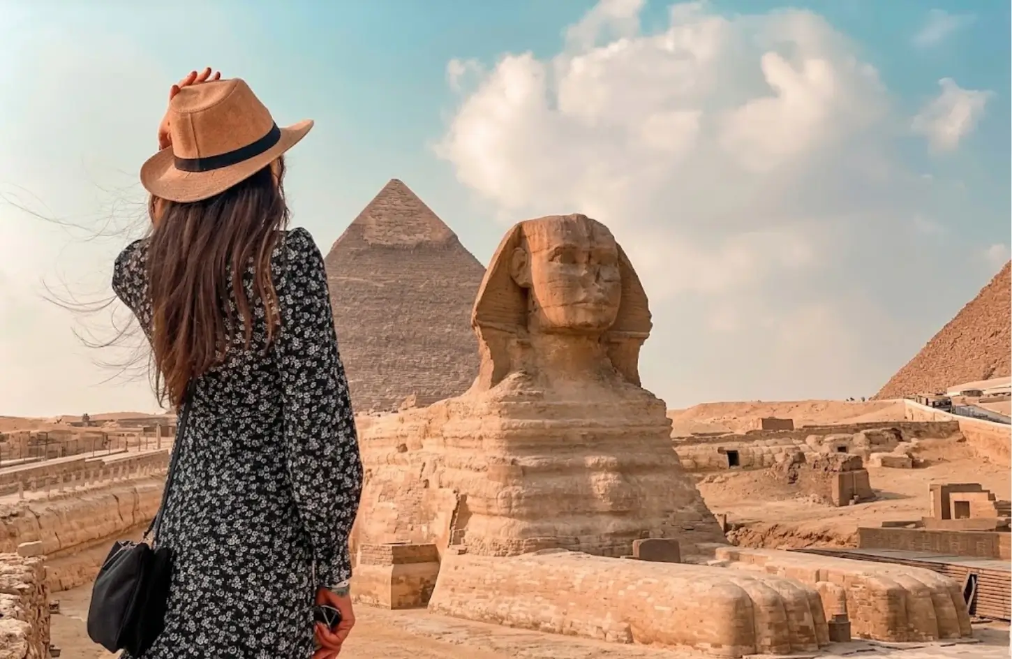 Female traveler in a hat and dress viewing the Great Sphinx and Pyramids of Giza during a trip to Egypt in February.