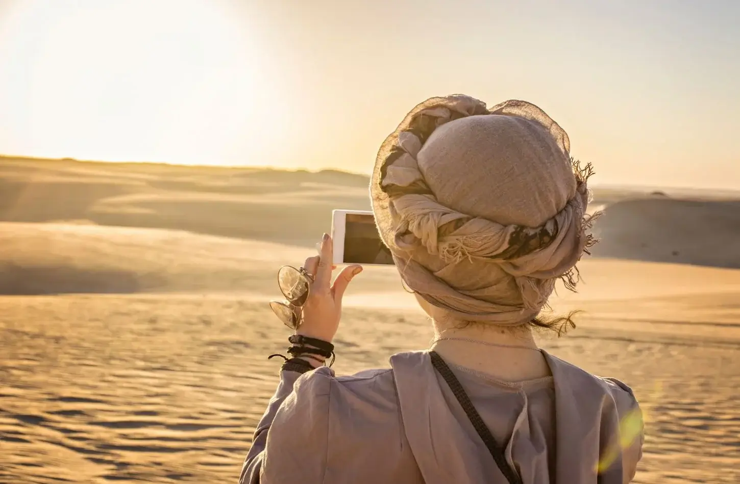 A traveler wearing a headscarf takes a photo with her smartphone of the golden sunset over the desert during a safari in Egypt in March.